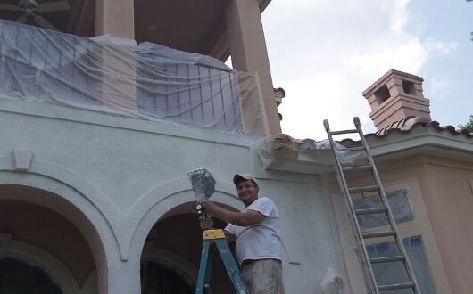 happy painter painting exterior of stucco house in The Woodlands Texas