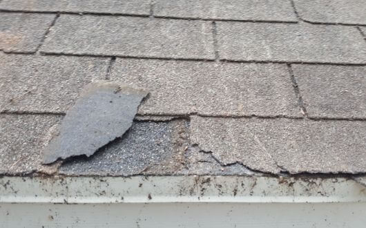 wind damaged roof with missing shingles in the front in The Woodlands, Texas